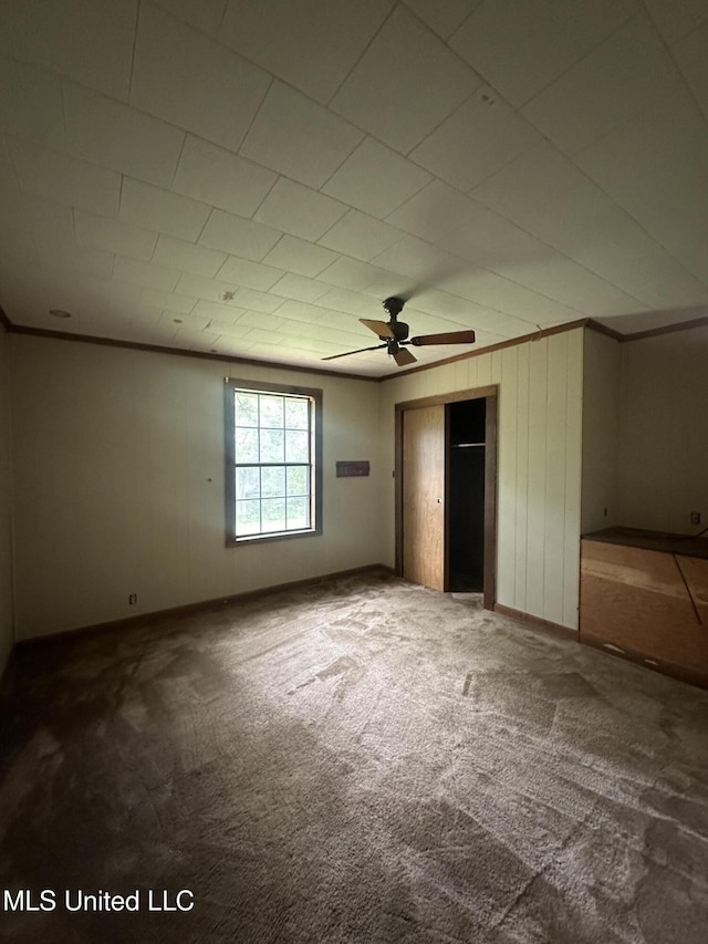 unfurnished bedroom featuring carpet floors, a closet, ornamental molding, baseboards, and a ceiling fan