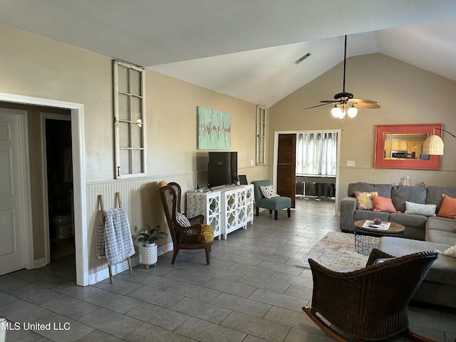 living room featuring a wainscoted wall, lofted ceiling, visible vents, and ceiling fan