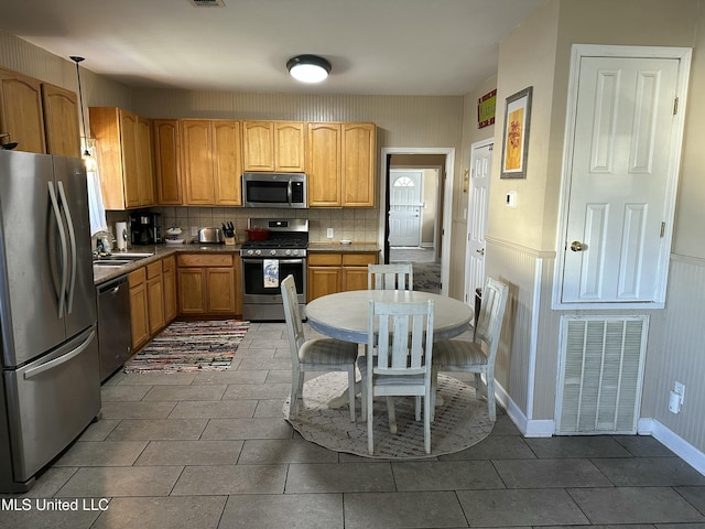 kitchen with visible vents, a wainscoted wall, a sink, backsplash, and stainless steel appliances