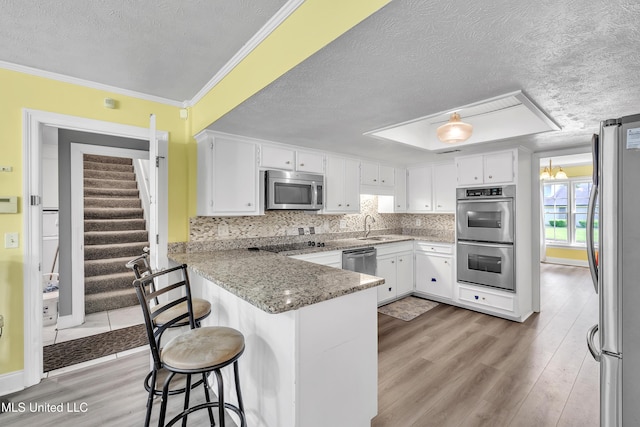 112 Rolling Meadows Dr, Jackson, MS 39211 - kitchen featuring appliances with stainless steel finishes, a textured ceiling, a peninsula, a sink, and light wood-style floors