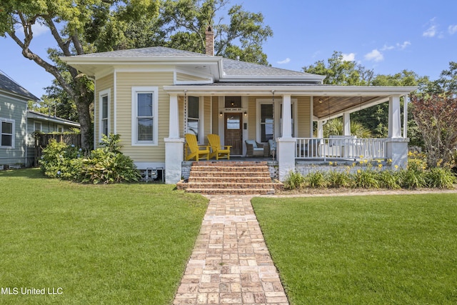 view of front of house featuring roof with shingles, a front yard, a chimney, and covered porch