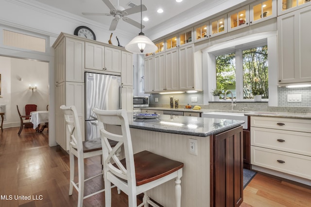 kitchen featuring a kitchen breakfast bar, backsplash, appliances with stainless steel finishes, a center island, and a sink