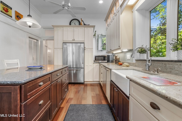 kitchen with hanging light fixtures, crown molding, appliances with stainless steel finishes, light hardwood / wood-style floors, and tasteful backsplash