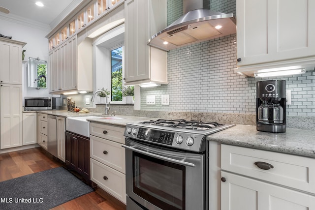 kitchen with wall chimney range hood, appliances with stainless steel finishes, white cabinetry, dark wood-type flooring, and crown molding