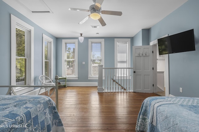 bedroom with a ceiling fan, attic access, visible vents, baseboards, and wood-type flooring