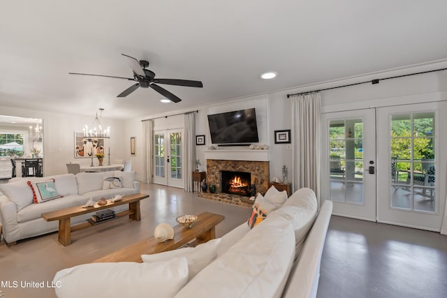 living room featuring a wealth of natural light, french doors, a stone fireplace, and ceiling fan with notable chandelier