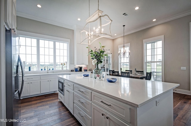 kitchen featuring white cabinets, hanging light fixtures, a kitchen island, dark wood-type flooring, and stainless steel appliances