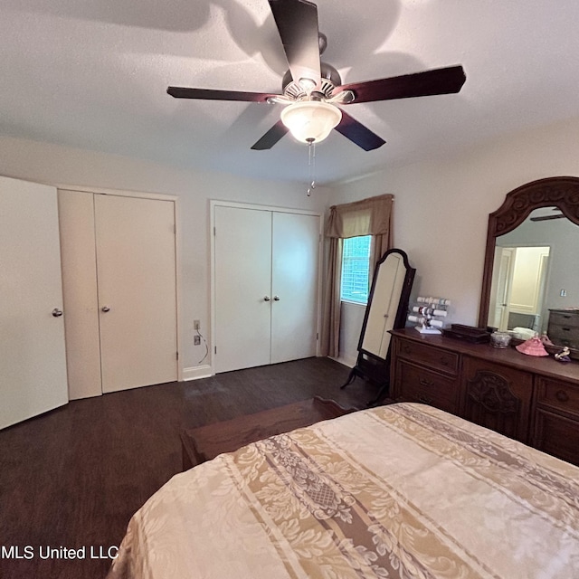 bedroom with two closets, dark wood-type flooring, and ceiling fan