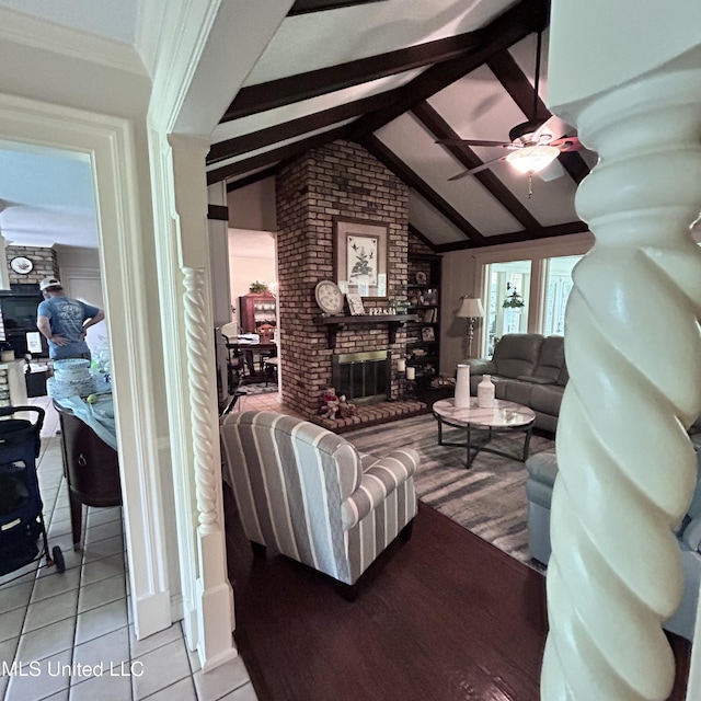 tiled living room featuring vaulted ceiling with beams, a fireplace, and ceiling fan