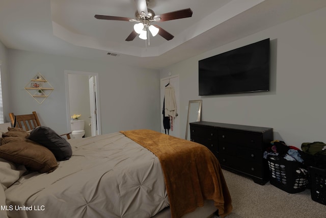 bedroom featuring light carpet, a tray ceiling, ceiling fan, and ensuite bathroom