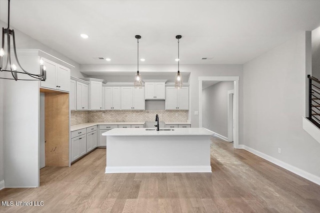 kitchen with decorative light fixtures, tasteful backsplash, an island with sink, sink, and white cabinets