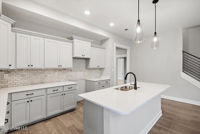 kitchen with hanging light fixtures, sink, a kitchen island with sink, and light hardwood / wood-style flooring