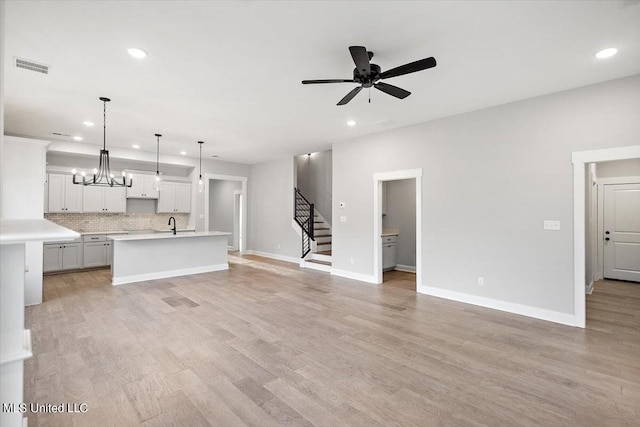 unfurnished living room featuring sink, ceiling fan with notable chandelier, and light wood-type flooring