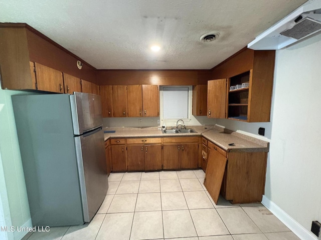 3435 Casa Grande Cir, Jackson, MS 39209 - kitchen with freestanding refrigerator, brown cabinets, a sink, under cabinet range hood, and a textured ceiling