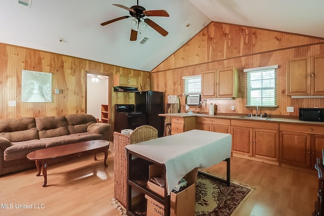 kitchen with ceiling fan, wooden walls, sink, black appliances, and light hardwood / wood-style floors