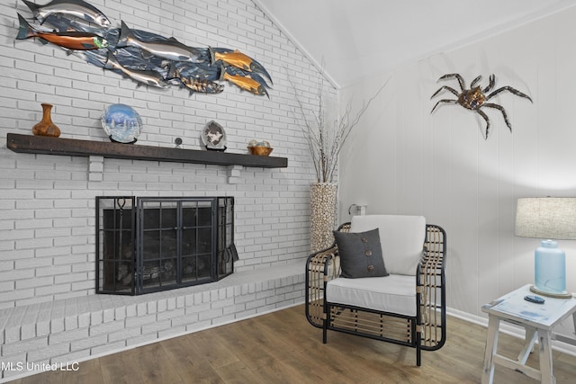 living area featuring vaulted ceiling, a brick fireplace, and wood finished floors