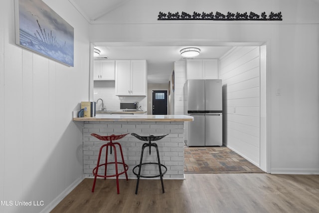 kitchen with a breakfast bar area, freestanding refrigerator, white cabinetry, wood finished floors, and a peninsula