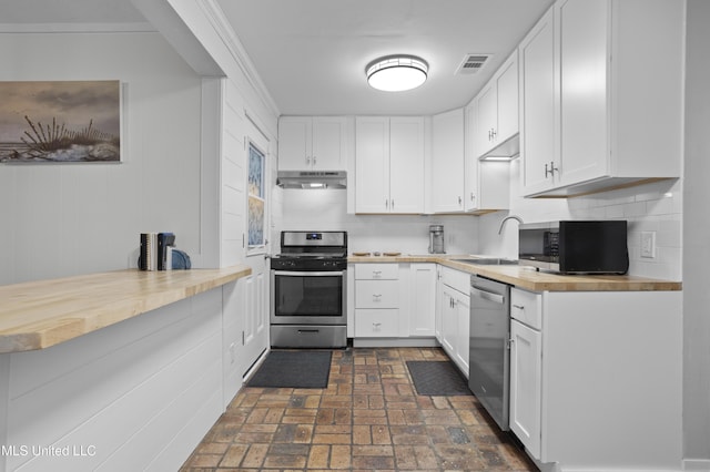 kitchen with brick floor, under cabinet range hood, wood counters, visible vents, and appliances with stainless steel finishes