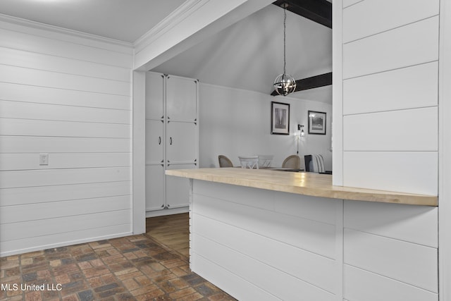 kitchen with brick floor, pendant lighting, ornamental molding, white cabinetry, and a kitchen bar