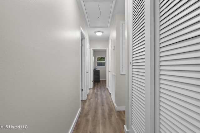 corridor featuring attic access, baseboards, and wood finished floors