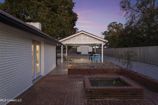 patio terrace at dusk with an outbuilding, a fenced backyard, and a storage unit