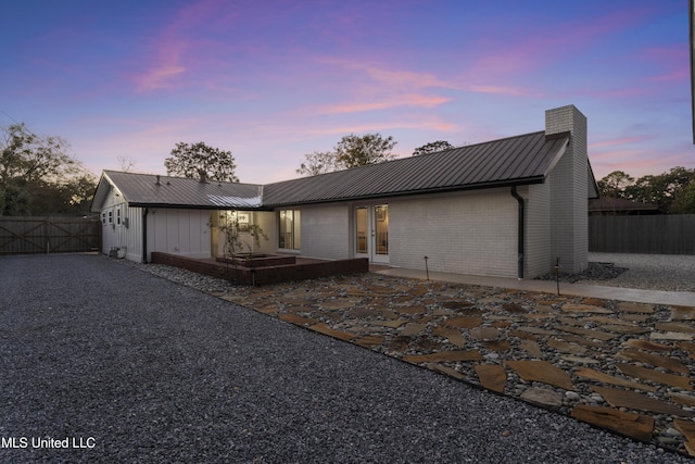 view of front of house featuring metal roof, fence, french doors, a chimney, and a patio area