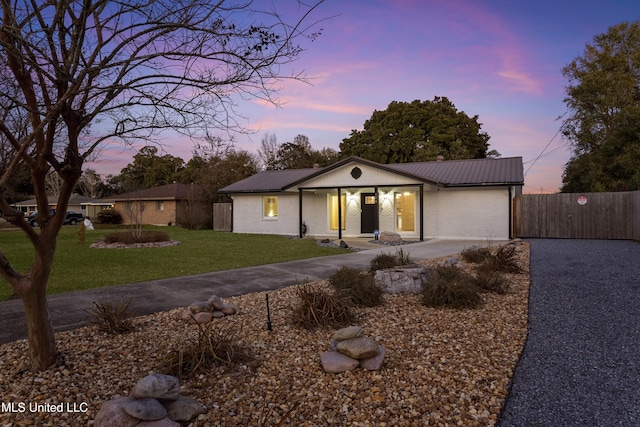 view of front of house with brick siding, a front yard, metal roof, fence, and driveway