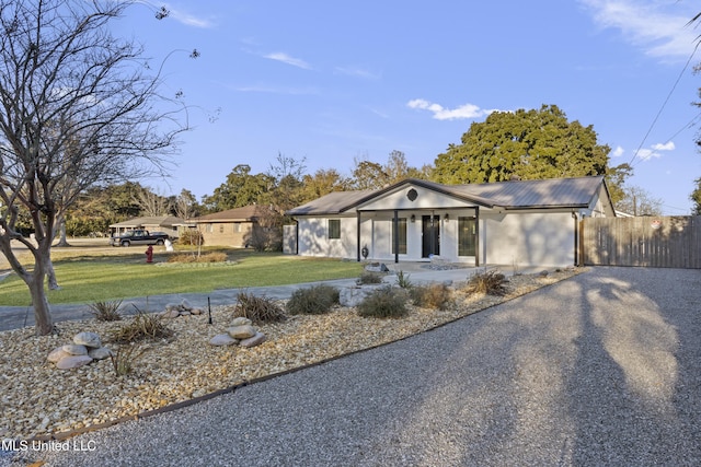 single story home featuring metal roof, driveway, a front yard, and fence