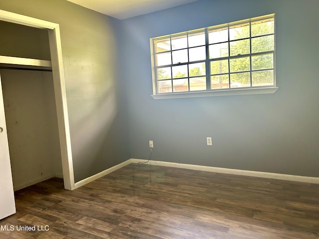 unfurnished bedroom featuring baseboards, dark wood finished floors, multiple windows, and a closet