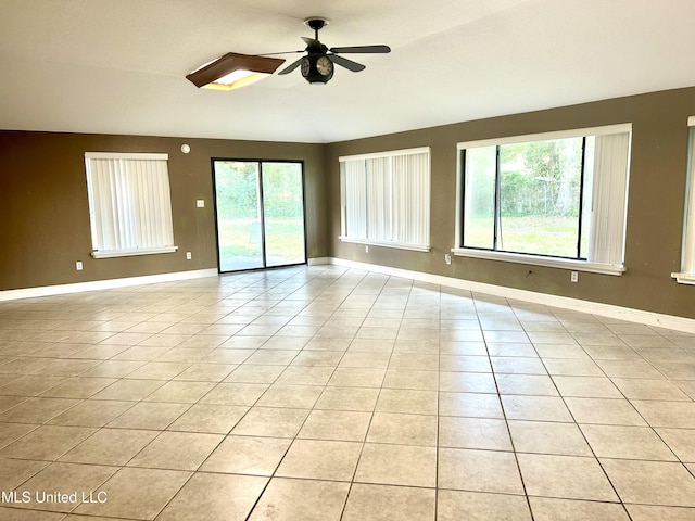 unfurnished room featuring plenty of natural light, a ceiling fan, baseboards, and light tile patterned flooring