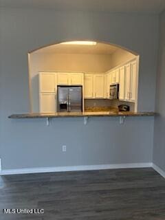 kitchen featuring arched walkways, baseboards, a breakfast bar, white cabinetry, and stainless steel refrigerator with ice dispenser