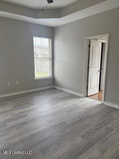 empty room featuring a tray ceiling, ceiling fan, baseboards, and wood finished floors