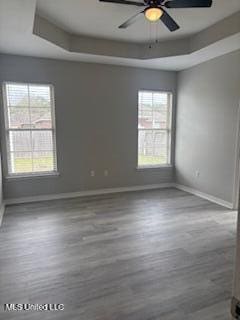 spare room featuring a ceiling fan, a tray ceiling, baseboards, and wood finished floors