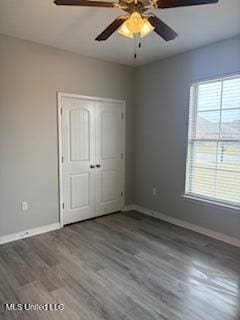 unfurnished bedroom with ceiling fan, a closet, wood finished floors, and baseboards