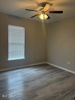 spare room featuring dark wood-style flooring, ceiling fan, and baseboards