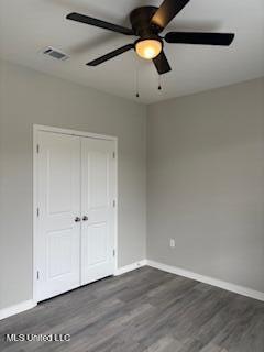 unfurnished bedroom with a closet, dark wood finished floors, visible vents, and baseboards