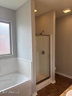 full bath featuring a stall shower, a garden tub, and baseboards