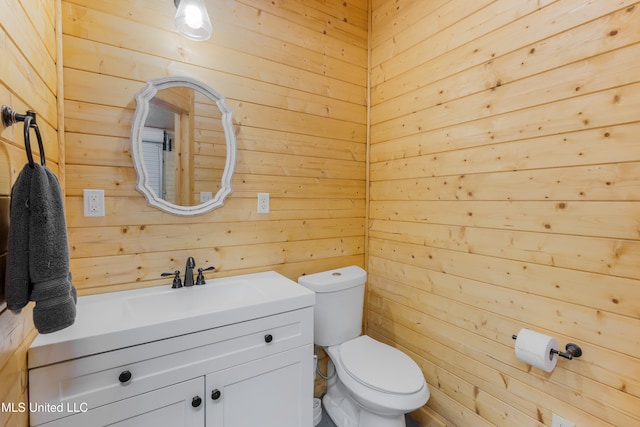 bathroom with vanity, toilet, and wood walls