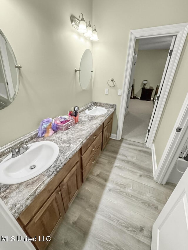 full bathroom featuring double vanity, wood finished floors, a sink, and baseboards