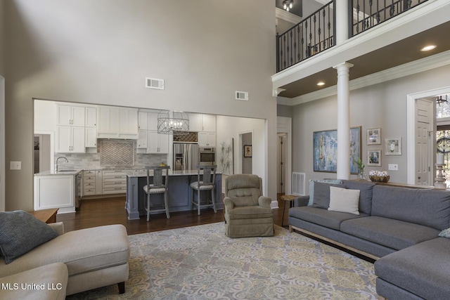 340 Sherborne Pl, Flowood, MS 39232 - living room with a high ceiling, a chandelier, dark wood-style flooring, ornamental molding, and decorative columns