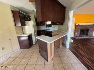 kitchen with light tile patterned flooring, a fireplace, white fridge, a kitchen bar, and kitchen peninsula