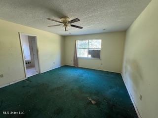 spare room featuring ceiling fan, dark carpet, and a textured ceiling