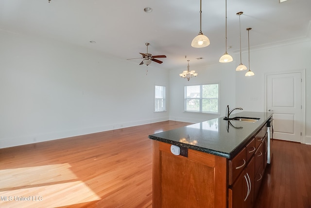 kitchen featuring wood finished floors, baseboards, a center island with sink, a sink, and ceiling fan with notable chandelier