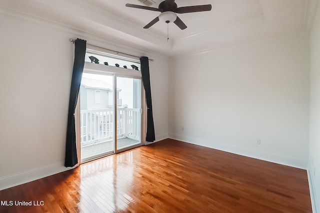 empty room featuring wood finished floors, baseboards, ornamental molding, ceiling fan, and a raised ceiling