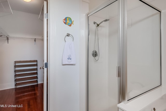 full bath with a spacious closet, a stall shower, and wood finished floors