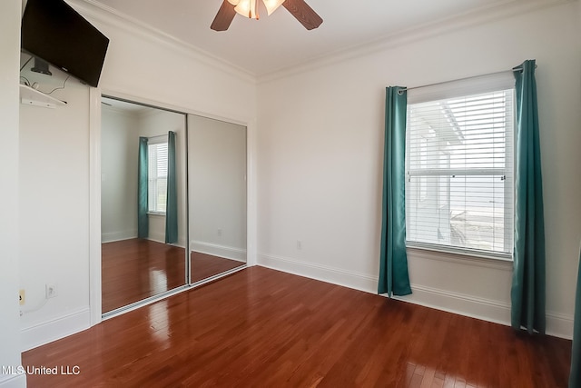 unfurnished bedroom featuring a ceiling fan, wood finished floors, baseboards, a closet, and crown molding