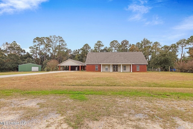 ranch-style home featuring covered porch, a front yard, concrete driveway, an outbuilding, and a carport