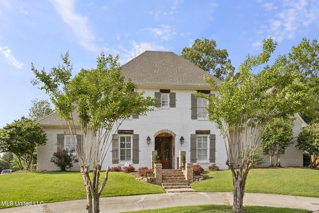 colonial home featuring roof with shingles, a front yard, and brick siding