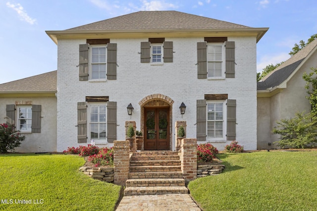 view of front facade featuring brick siding, a shingled roof, a front lawn, and french doors