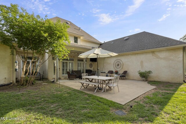 back of property with a shingled roof, a patio area, stucco siding, and a yard